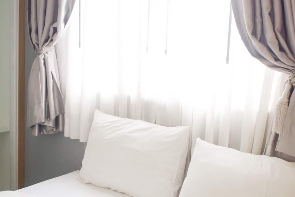 A bed with white linens, a window with sheer curtains, and a door with a curtain.