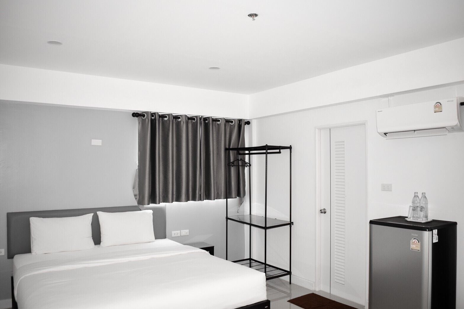 Una habitación de hotel moderna con cama, armario, kitchenette pequeña y aire acondicionado instalado en el techo.