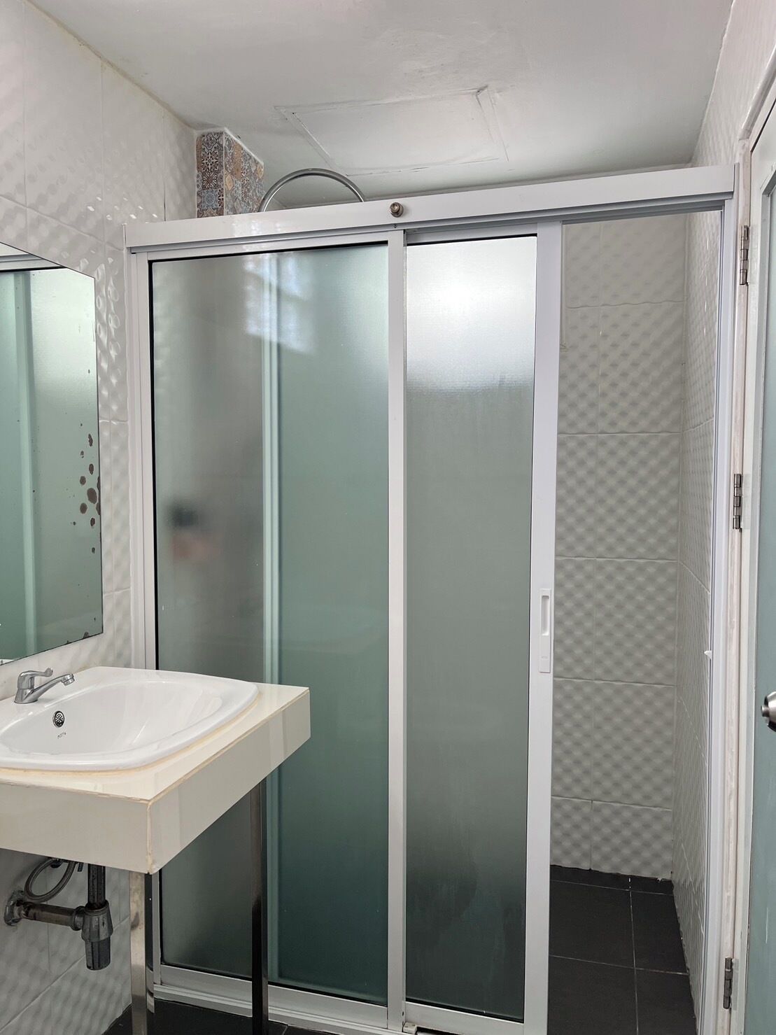 A bathroom with a white sink, a glass shower enclosure, and a tiled floor.
