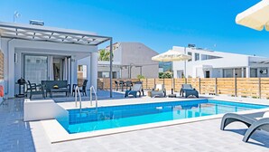 Un área de piscina moderna al aire libre con sillones de descanso y una zona de estar cubierta.