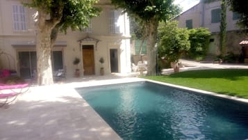 Relax by the serene pool surrounded by lush greenery and a classic building with a charming balcony.