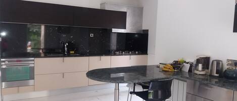 A modern kitchen with a black countertop, stainless steel appliances, and a round dining table with bar stools.