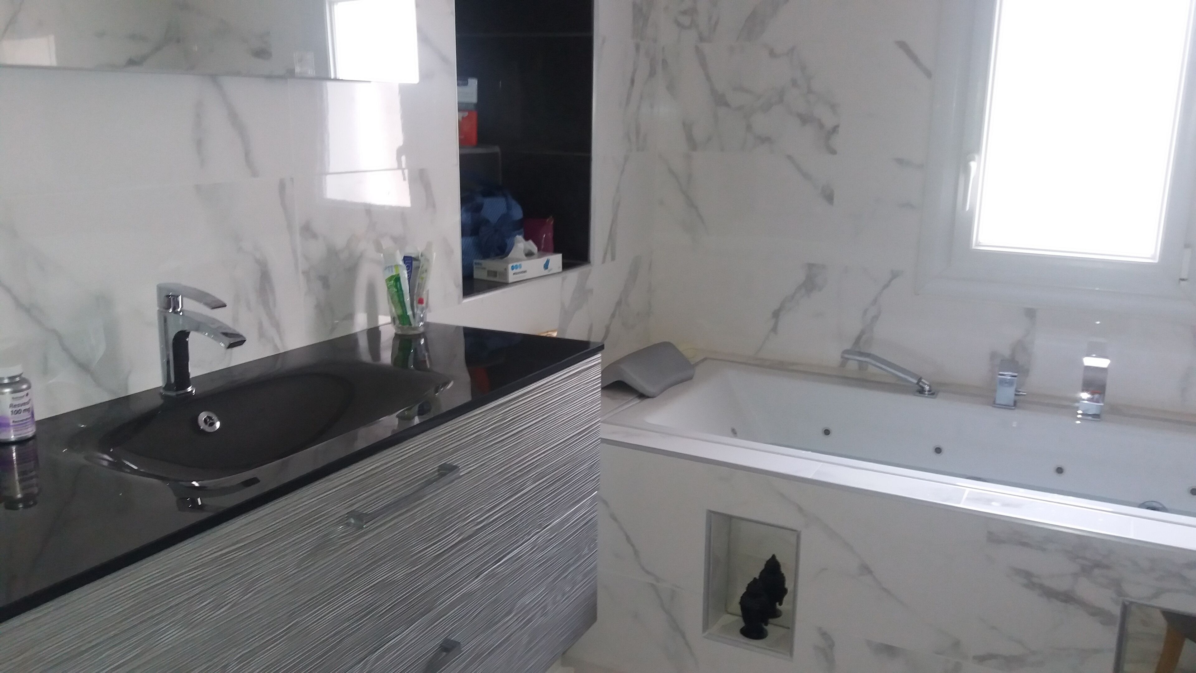 A modern bathroom with a black sink, a mirror, a bathtub, and a window.