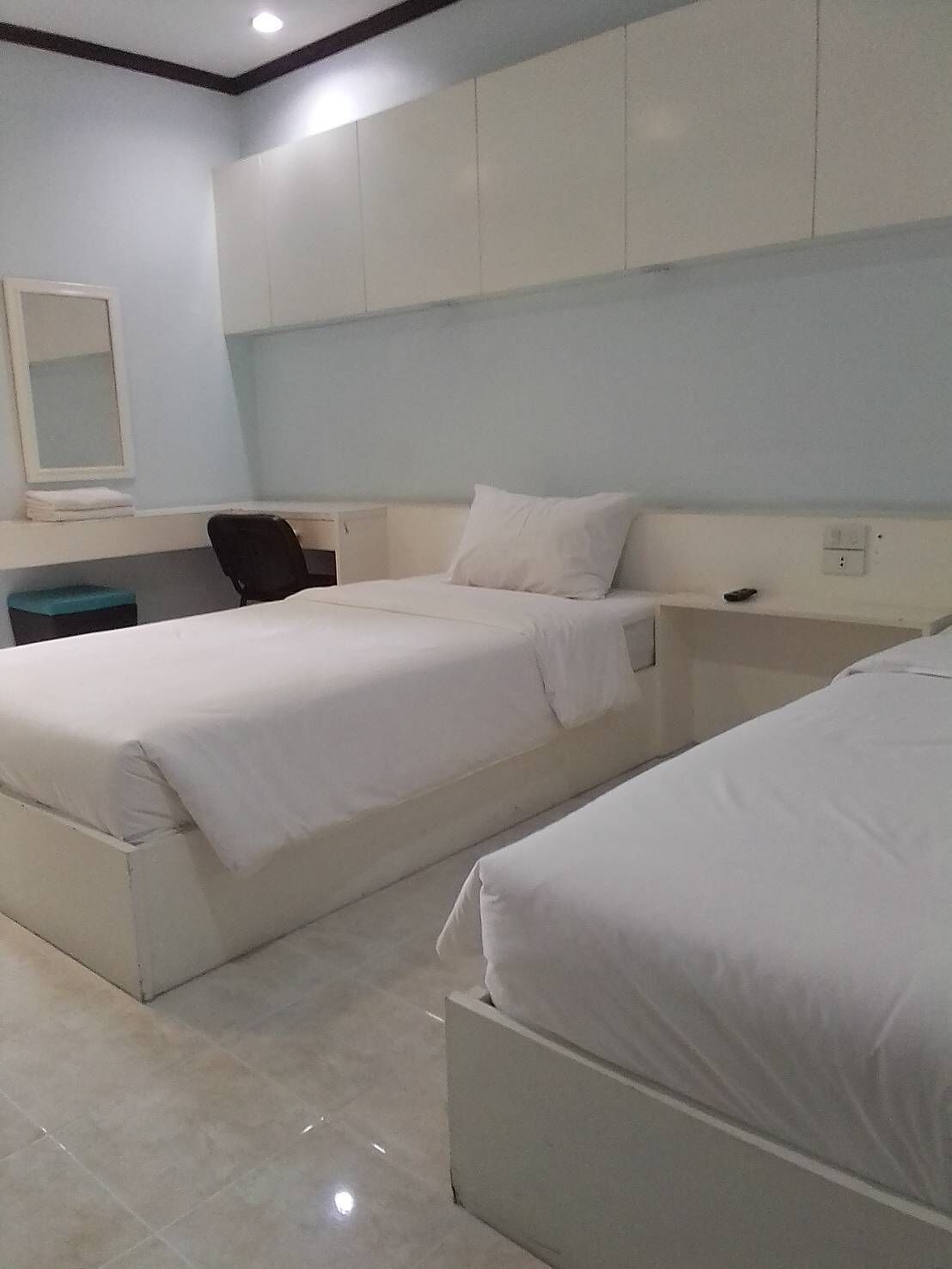 A hotel room with two beds, a desk, a chair, and a mirror.