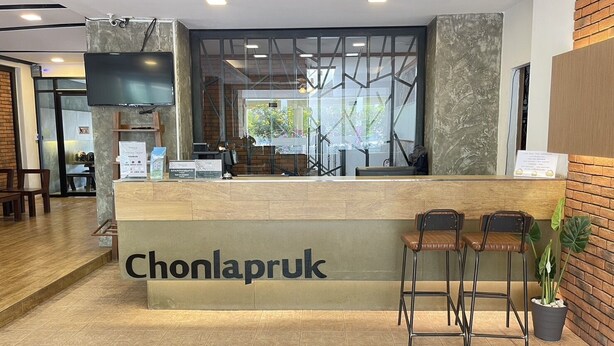 A reception area with a wooden counter, two bar stools, a flat-screen TV, and a glass partition. - Chonlapruk Lakeside Hotel (Khon Kaen)