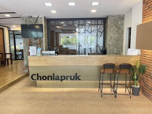 A reception area with a wooden counter, two bar stools, a flat-screen TV, and a glass partition.