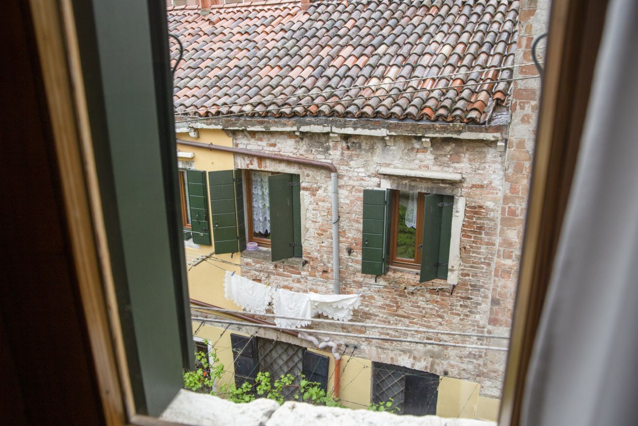 A view of a building with a tiled roof and brick walls, featuring two windows with green shutters and a balcony with clothes hanging.