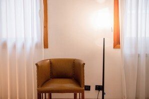 Une pièce comprenant un seul fauteuil en cuir marron, un lampadaire et un mur blanc avec une prise de courant.