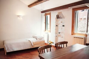 A small, cozy room with a wooden bed, a dining table, and a bookshelf.