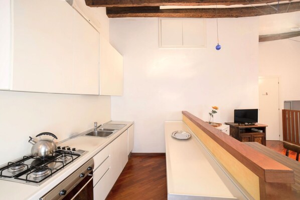 Une cuisine de taille réduite, équipée d’une cuisinière à gaz, d’un évier et de meubles de rangement en bois.
