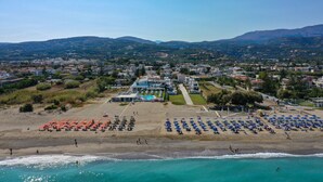 A coastal resort with beach umbrellas, a swimming pool, and a view of the surrounding hills. - Blue oyster Beachfront villa, No car needed 1 (Rethymno)