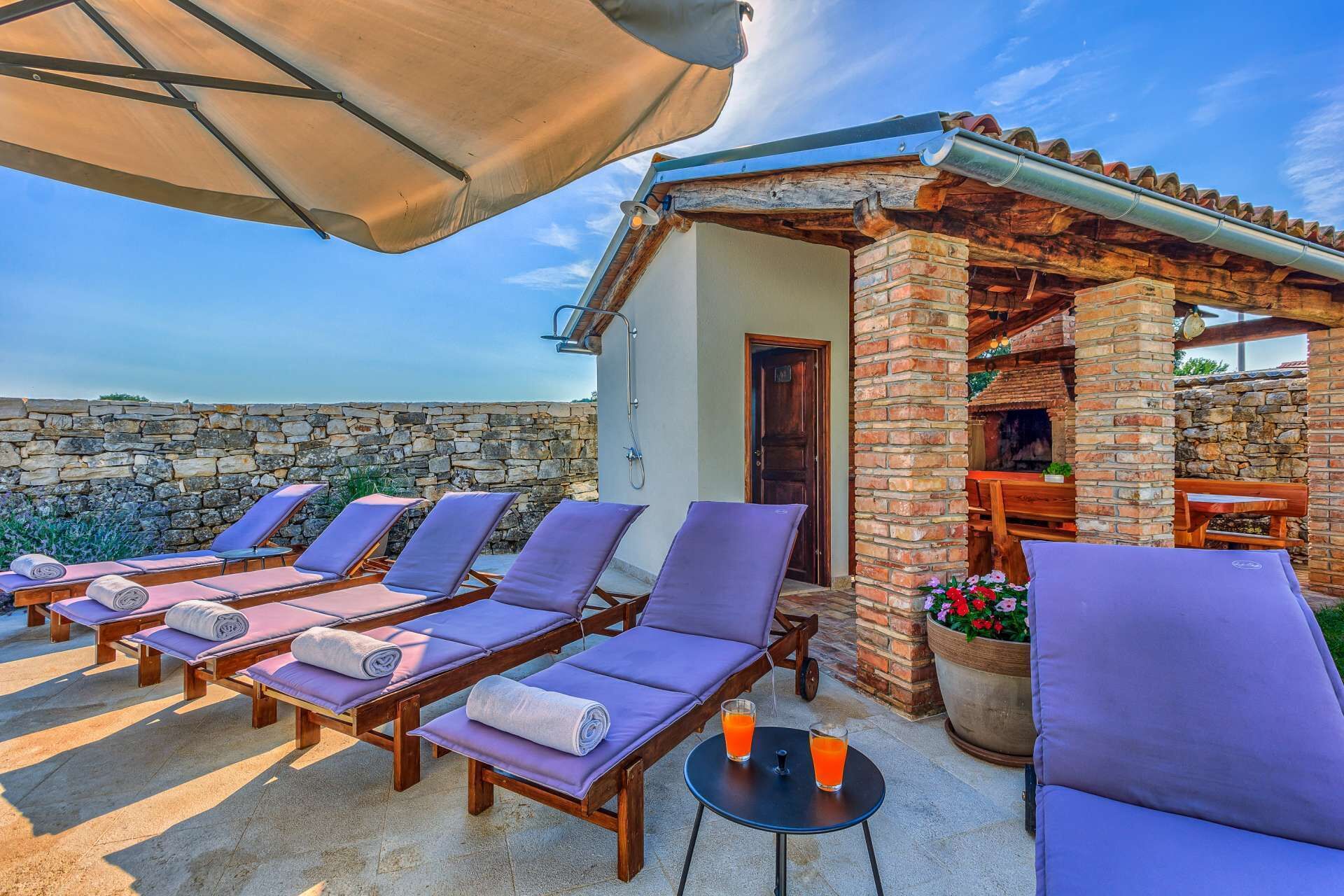 A sunlit outdoor seating area with wooden loungers and a stone wall backdrop.