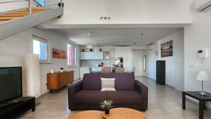Una sala de estar moderna con un sofá, dos mesas de centro, un televisor y una escalera que sube a un nivel superior.