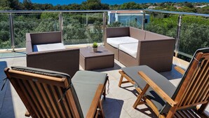 Un balcón con mobiliario de mimbre, una mesita y vistas al mar y la vegetación.