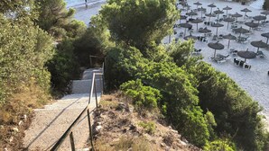 Zona costera con playa, sombrillas y una escalera que baja a la playa.
