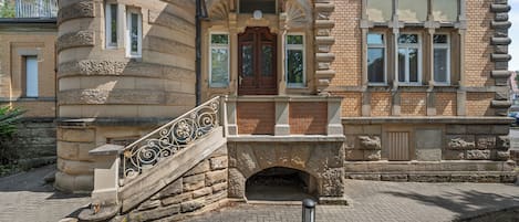 A historic building with a stone staircase leading to a wooden door, brick walls, and a stone balustrade.