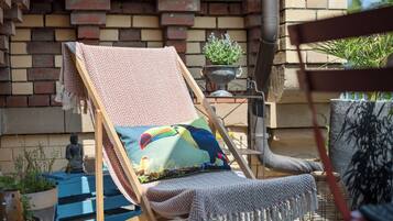 Ein bequemer Holzloungesessel mit farbenfroher Kissenauflage, ein kleiner Topfpflanze und eine Buddha-Statue im Hintergrund.