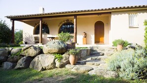 Una casa amb façana de pedra, grans finestres i un porxo cobert amb seients exteriors.