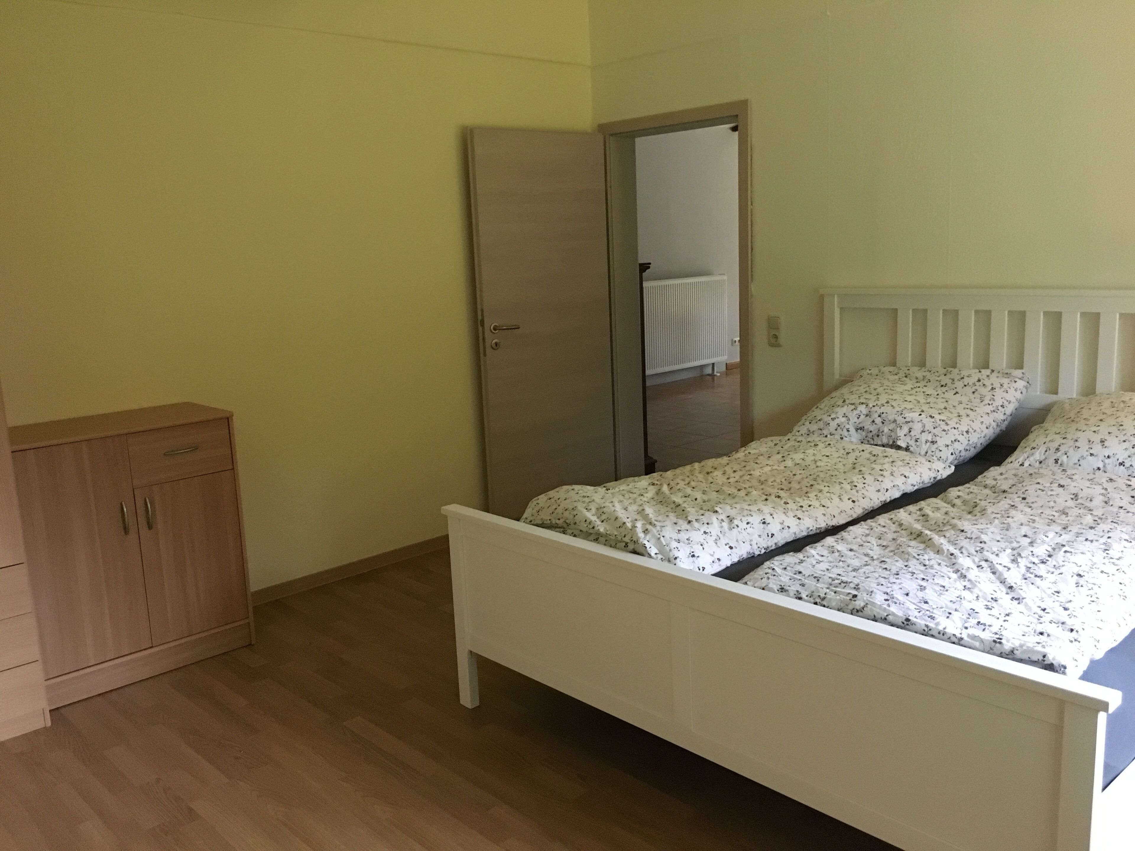 Un dormitorio con una cama individual, un armario de madera y una puerta que da a otra habitación.