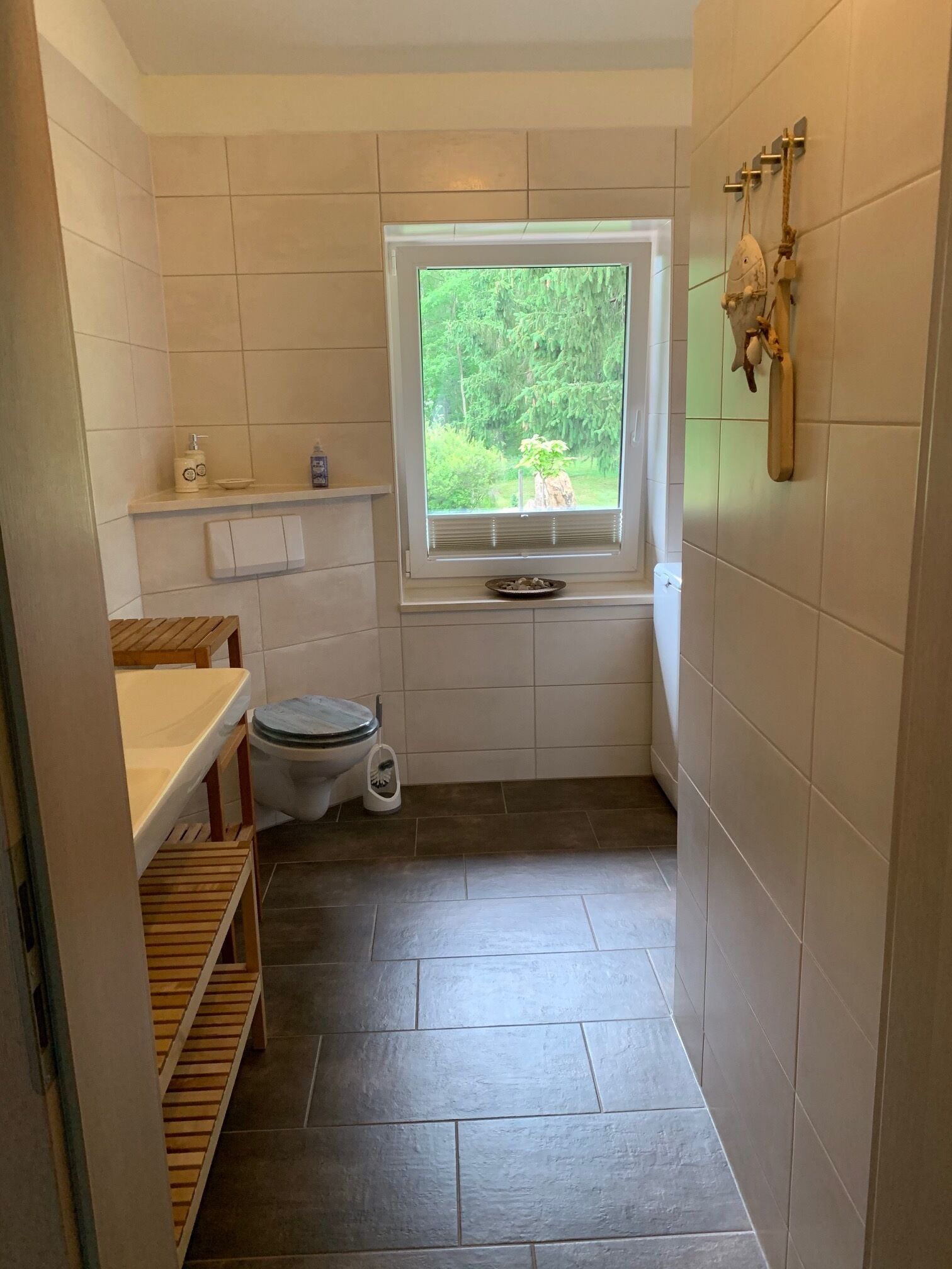 A compact bathroom with a toilet, a window with a view of greenery, and a shelf with toiletries.
