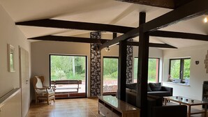 A spacious living area with a large window, a sofa, a wooden cabinet, and a bench. - Standalone idyllic holiday home in the middle of nature for 6 to 8 people (Grabow)