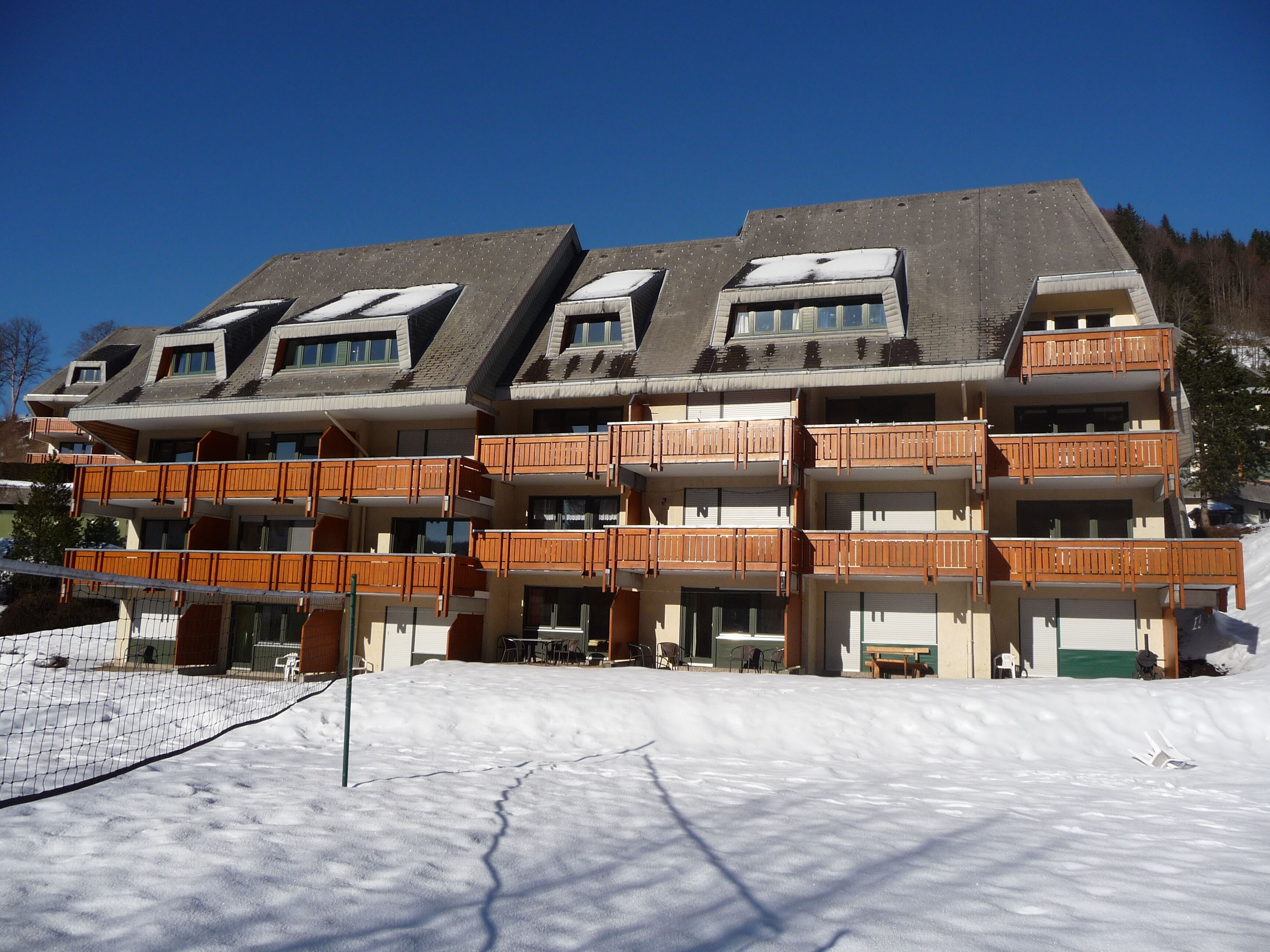 Ein mehrstöckiges Hotel mit Balkonen, im Hintergrund eine Skipiste und ein klarer, blauer Himmel.