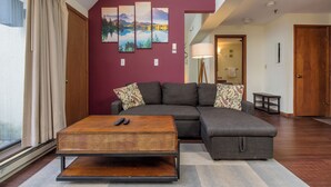 Un salon comprenant un canapé d’angle, une table basse en bois et une grande fenêtre avec des rideaux.