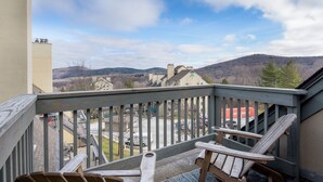 Un balcon avec des chaises en bois, une vue sur un parking et des montagnes lointaines.