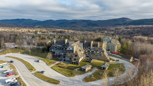 Un complexe d’appartements moderne composé de plusieurs immeubles, doté d’un parking et offrant une vue sur les montagnes environnantes.