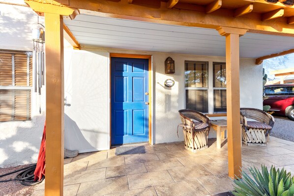 A covered porch with a blue door, outdoor seating, and a garden area.