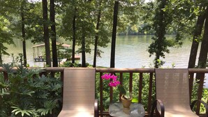 A wooden deck with two chairs and a table, overlooking a calm lake with trees and a dock in the background. - Quiet, Charming Lake Front Home with Kayaks, 2 Guest Maximum (Hot Springs)