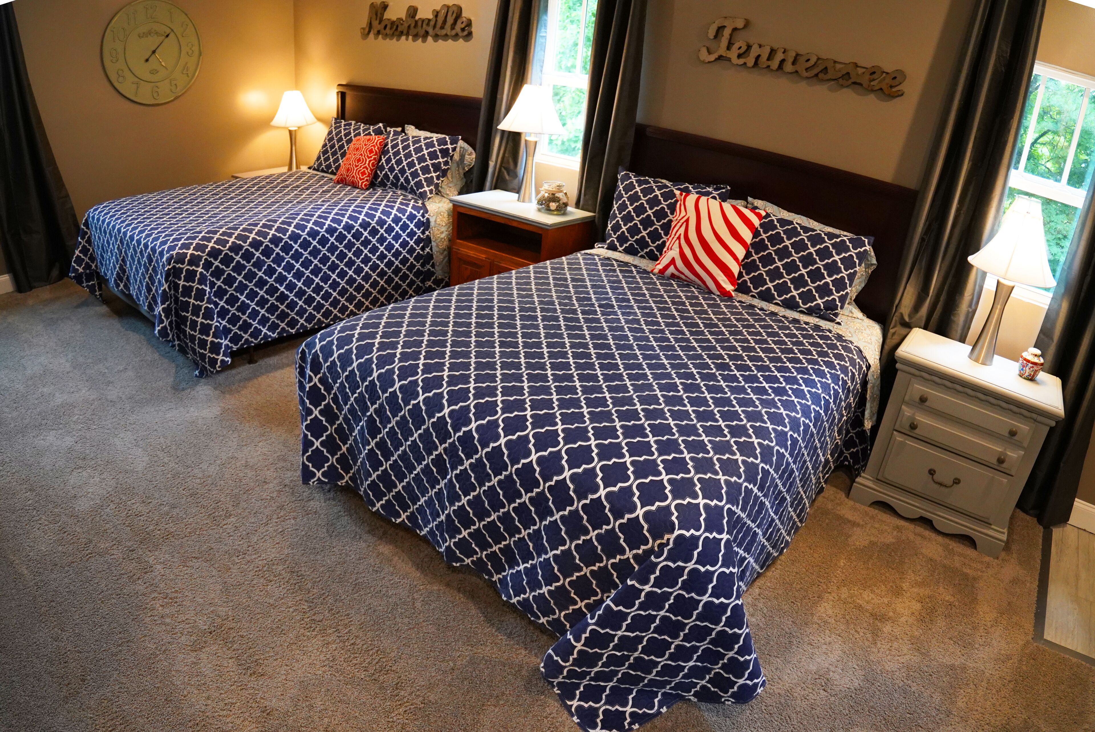 A hotel room with two beds, each with a patterned bedspread, a nightstand with a lamp, and a wall clock.