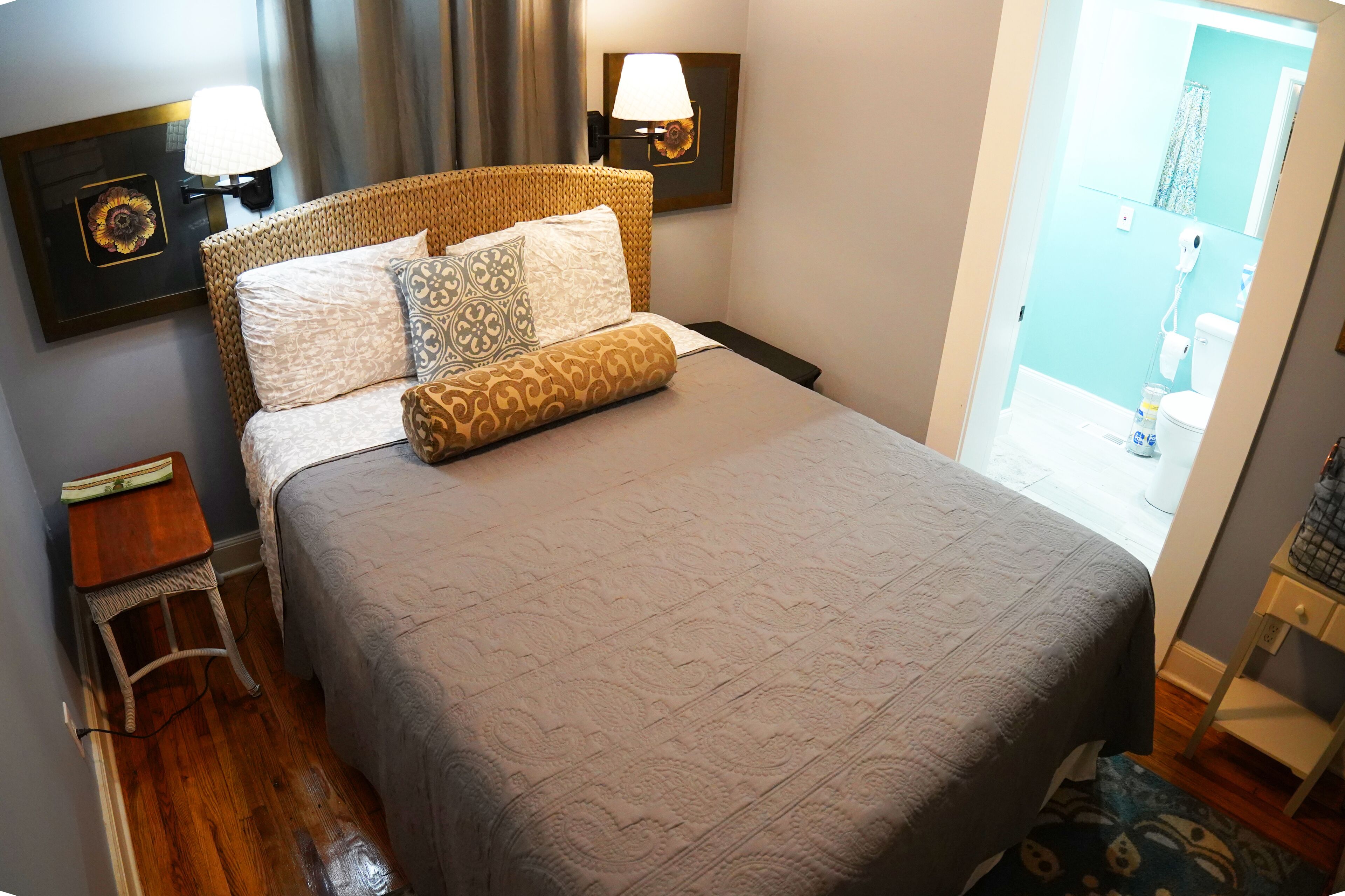 A neatly made bed with patterned bedding, a bedside table with a lamp, and a wall-mounted picture frame.