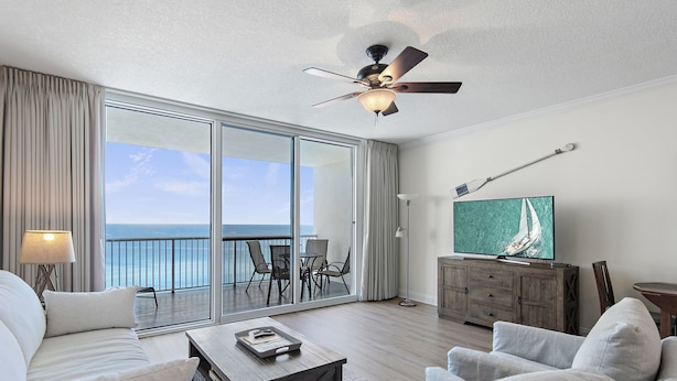 A spacious living room with a large sliding glass door leading to a balcony with a view of the ocean. - Oceanfront Romantic Getaway-Including Free Beach Chair Service! (Panama City Beach)