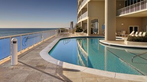 A poolside area with a clear view of the ocean, a pool, and a building with balconies. - Oceanfront Romantic Getaway-Including Free Beach Chair Service! (Panama City Beach)