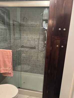 A glass-enclosed shower with a handheld showerhead, a glass door, and a pink towel hanging on a rack.