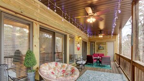 A covered porch with a ceiling fan, string lights, a round chair, a table, and a small potted plant.