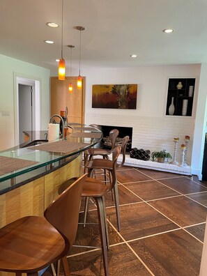 Une cuisine moderne dotée d’un îlot central en verre, de tabourets de bar, de luminaires suspendus et d’une cheminée.