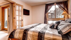 A bedroom with a large bed, a television on the wall, and a window with curtains. - Best Location in Town -- One Block to Main St. & Close to the Slopes and Gondola (Breckenridge)
