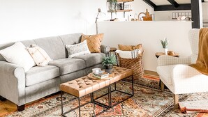 A living room with a grey sofa, a wooden coffee table, a patterned rug, and a white armchair.