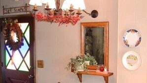 Un coin repas avec une table en bois, des chaises, un lustre, une étagère fixée au mur ornée d’une plante, et une porte décorée d’une guirlande.