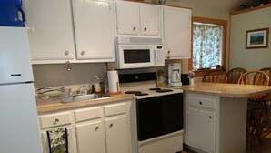 A compact kitchen with white cabinets, a microwave, a stove, and a coffee maker. -  A Little Piece Of Heaven (Brownville)