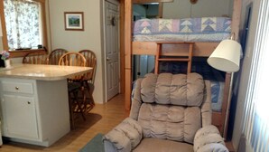 A compact living space with a bunk bed, a cushioned chair, a small kitchen area, and a dining table. -  A Little Piece Of Heaven (Brownville)