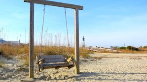 Une balançoire en bois installée sur une plage de sable, avec un phare en arrière-plan.