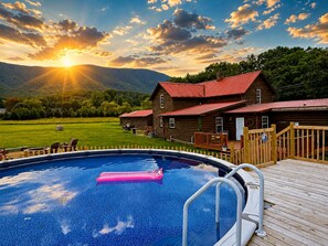 A wooden cabin with a swimming pool, surrounded by a deck and a grassy field.