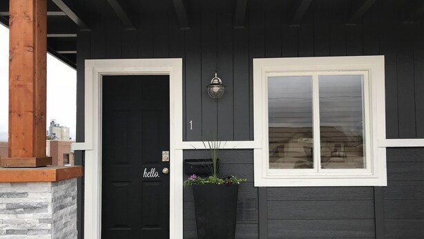 A black house with a white door and window, a stone pillar, and a black planter with flowers. - Cut Bank Unit #1 near Glacier National Park! (Cut Bank)