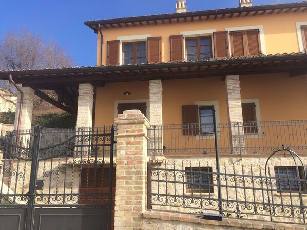 A two-story building with a balcony, a gated entrance, and a brick chimney. - Old Country House and pool In Umbrian Hills Between Foligno And Assisi (Foligno)