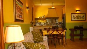 A cozy living room with a sofa, a dining table with chairs, a kitchen area with a tiled backsplash, and a hanging light fixture. - Old Country House and pool In Umbrian Hills Between Foligno And Assisi (Foligno)