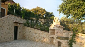 A stone building with a chimney, a paved courtyard, and a metal fence. - Old Country House and pool In Umbrian Hills Between Foligno And Assisi (Foligno)