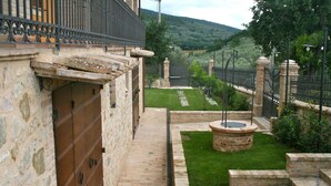 A courtyard with a brick wall, a wooden door, a small garden area with a circular water feature, and a metal fence. - Old Country House and pool In Umbrian Hills Between Foligno And Assisi (Foligno)